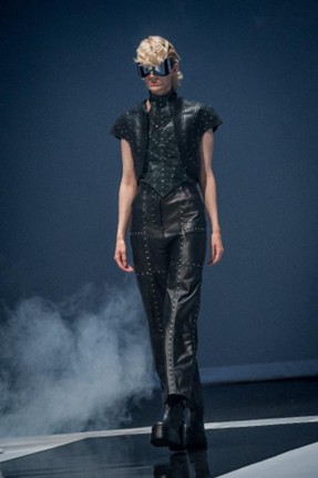 Runway model in black studded leather vest and pants with futuristic sunglasses.