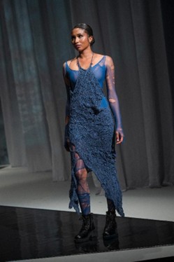 Runway model in a blue distressed dress layered over a sheer blue bodysuit.