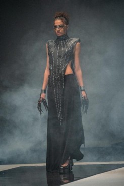 Runway model in a long black dress with studded leather bodice and claw-like gloves.