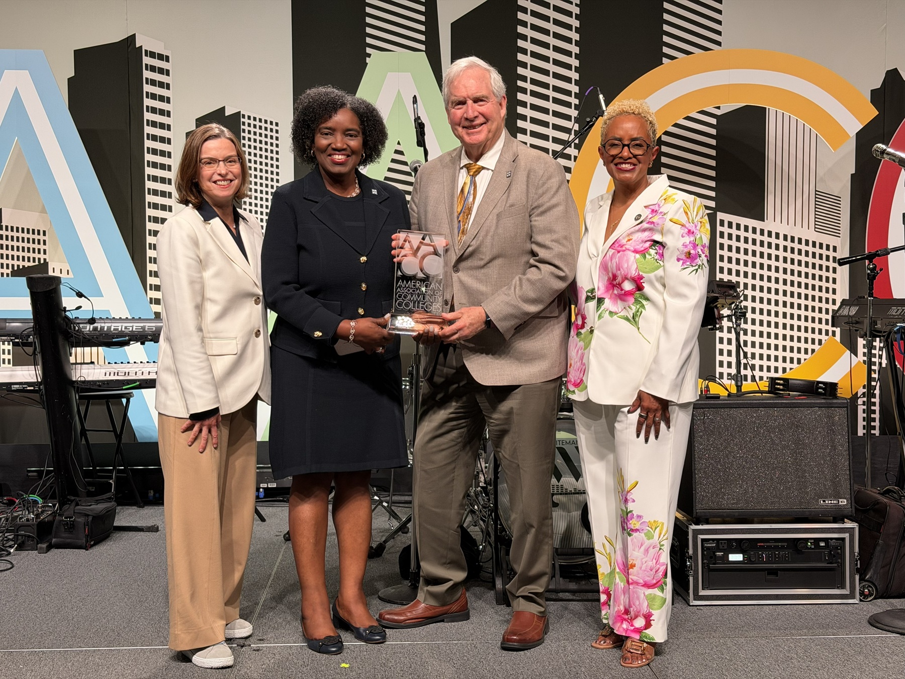 Dr. Leigh Goodson, chair of the AACC Board of Directors; Dr. Avis Proctor, Harper president; William Kelley, chair of the Harper Board of Trustees; and Dr. DeRionne Pollard, AACC president/CEO stand holding an award at a gala.