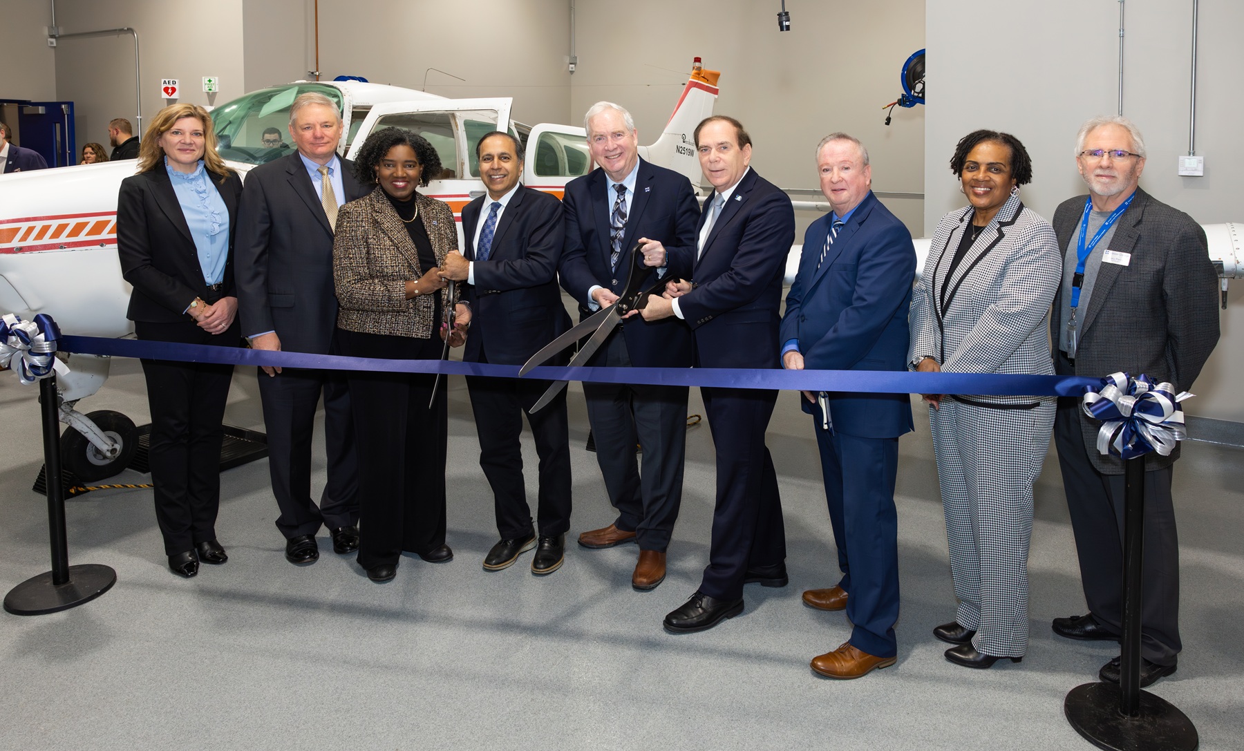 Leaders from Harper College, elected officials and members of the Harper College Board of Trustees cut a ribbon in front of an airplane in the Aviation Maintenance Lab.