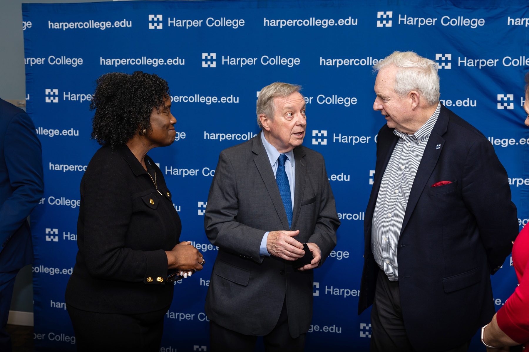 Dr. Avis Proctor, Sen. Dick Durbin and Board Chait Bill Kelley talk in front of a Harper College banner.