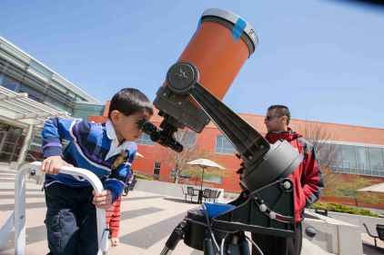 A young student looks through a telescope at Harper's College and Career Expo