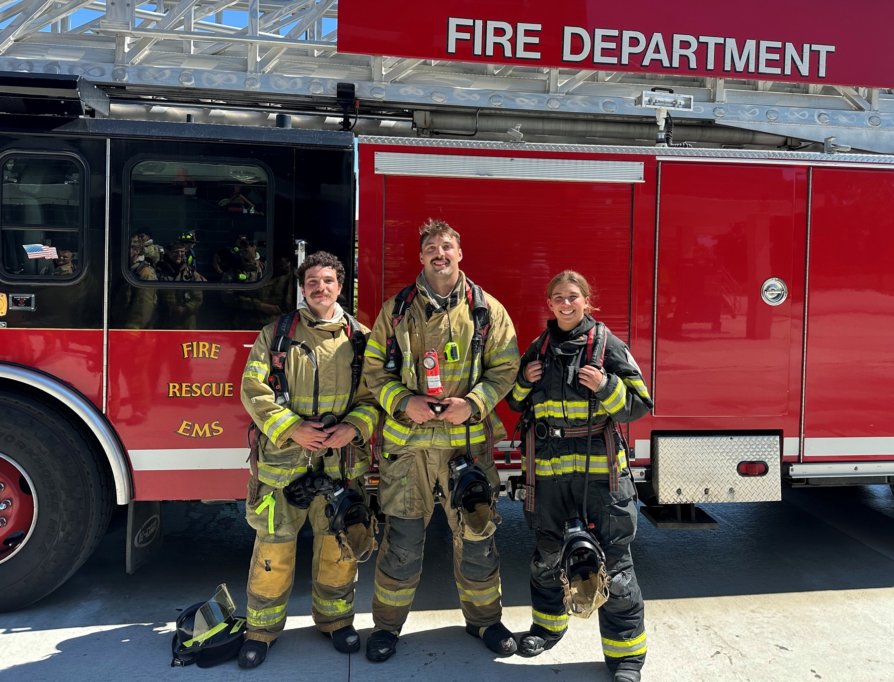 Three Harper Fire Academy students stand in front of a fire truck during their training course