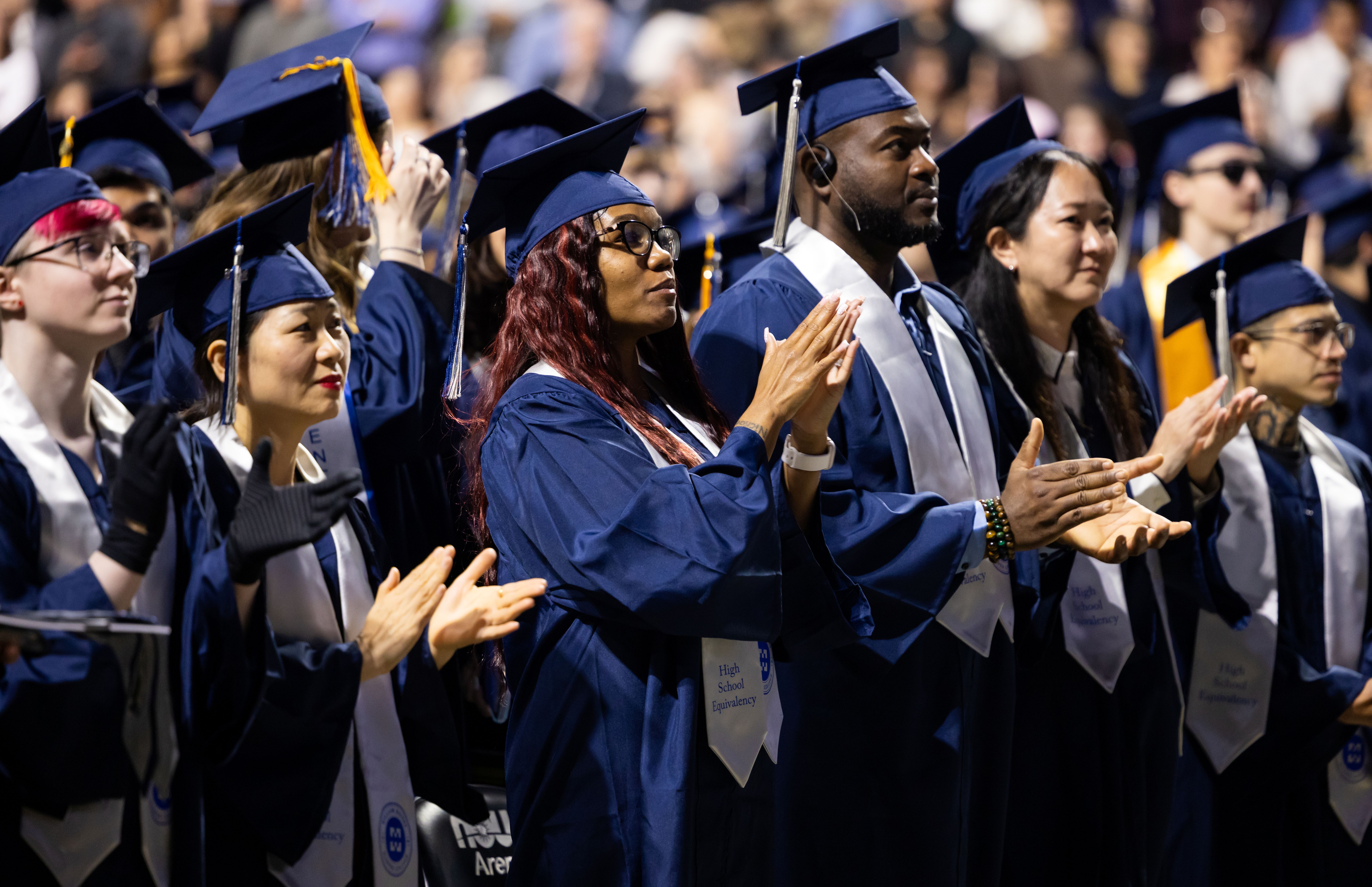 Several Harper College graduates stand and applaud at the Commencement ceremony
