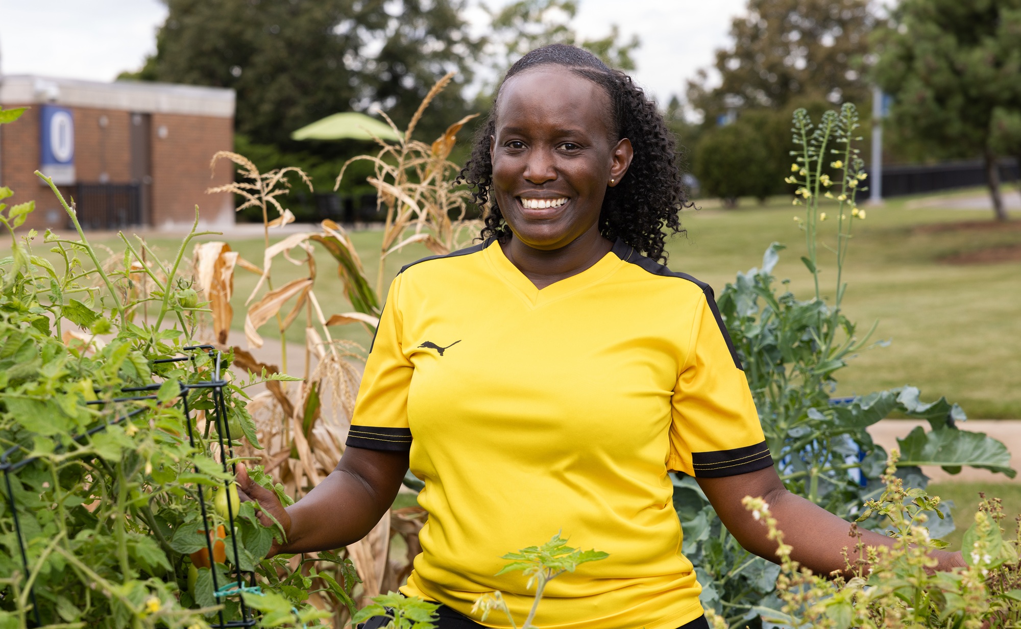 Edith Mugisha, a Harper student, stands amidst tall plants in the Harper Grows Community Garden