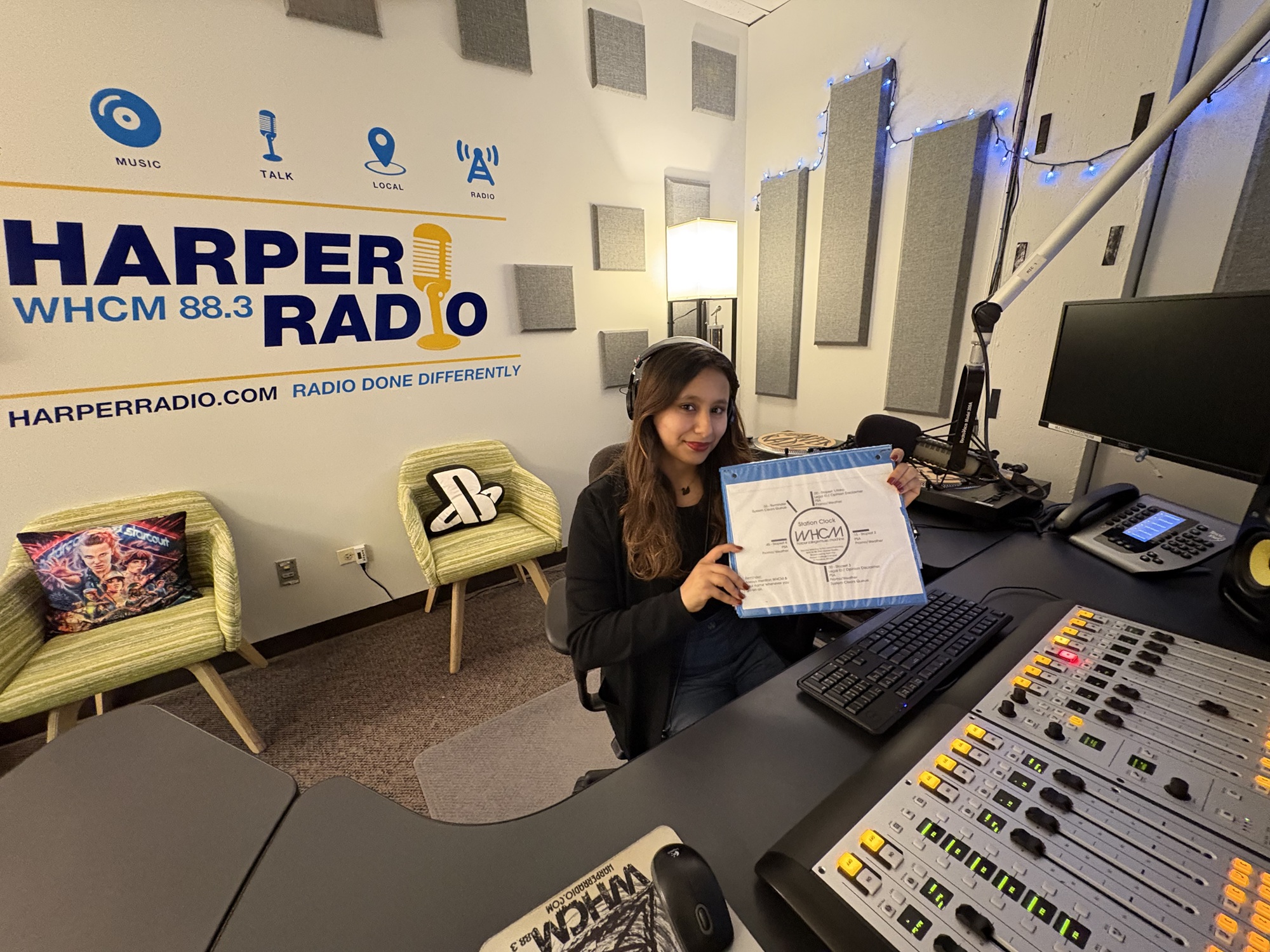 Harper student Abeer Abu Ghalyoun sits in the WHCM broadcast booth with the Harper Radio logo behind her