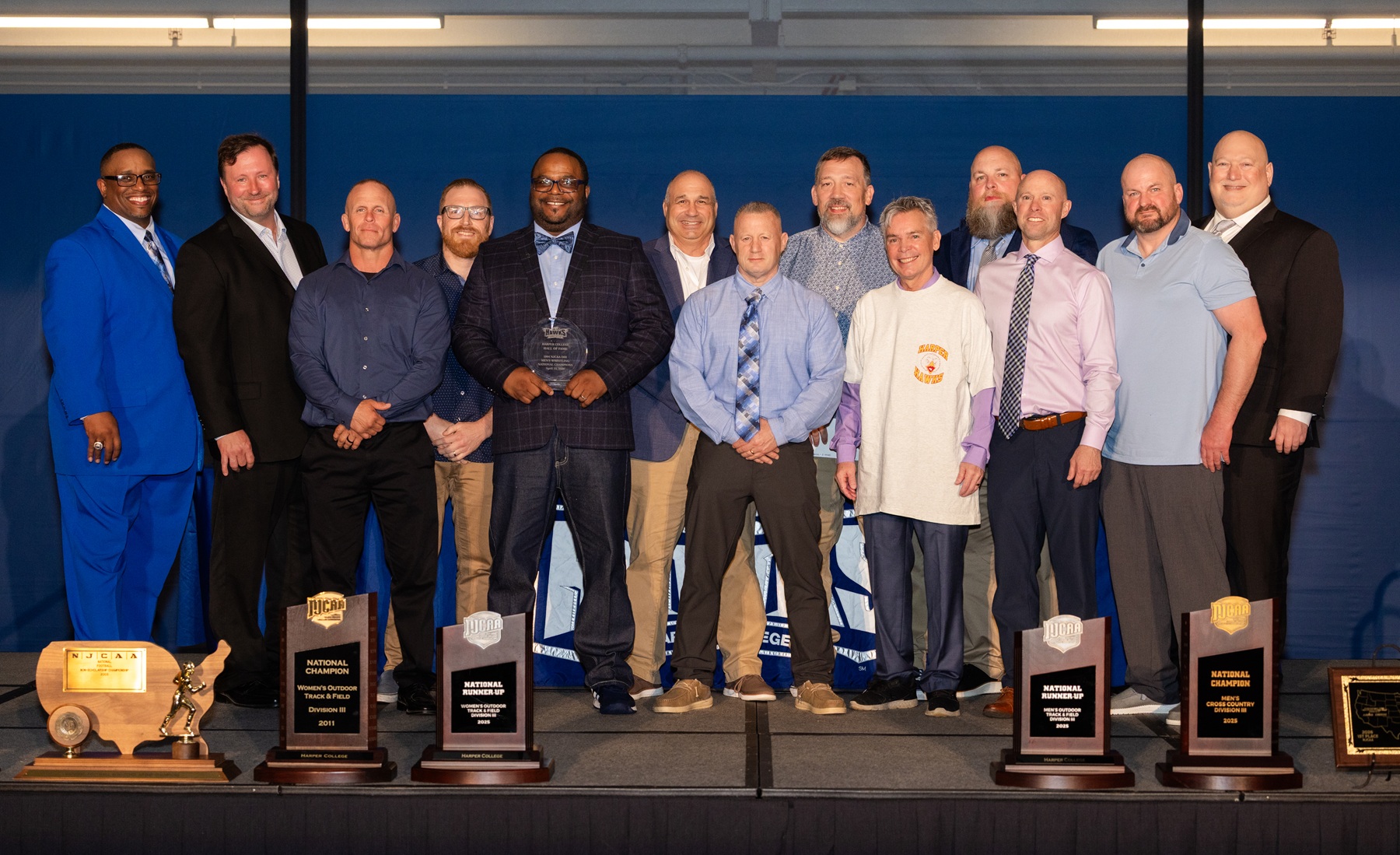Members and coaches from the 1994 Harper College Men's Wrestling Team stand on a stage after being inducted into the Harper Athletics Hall of Fame.