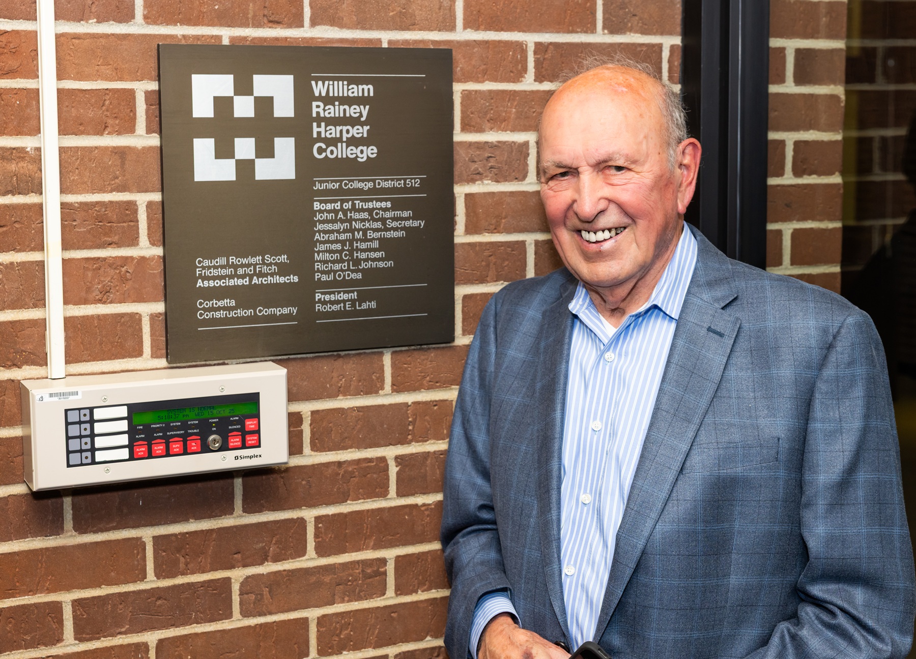 Founding Harper College Trustee James Hamill stands next to a plaque in Building A that bears his name and the names of his fellow trustees.