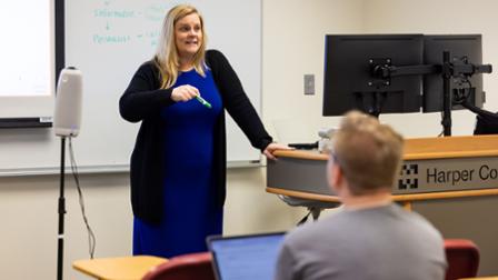 Dr. Stephanie Whalen stands before a whiteboard to teach a course at Harper College