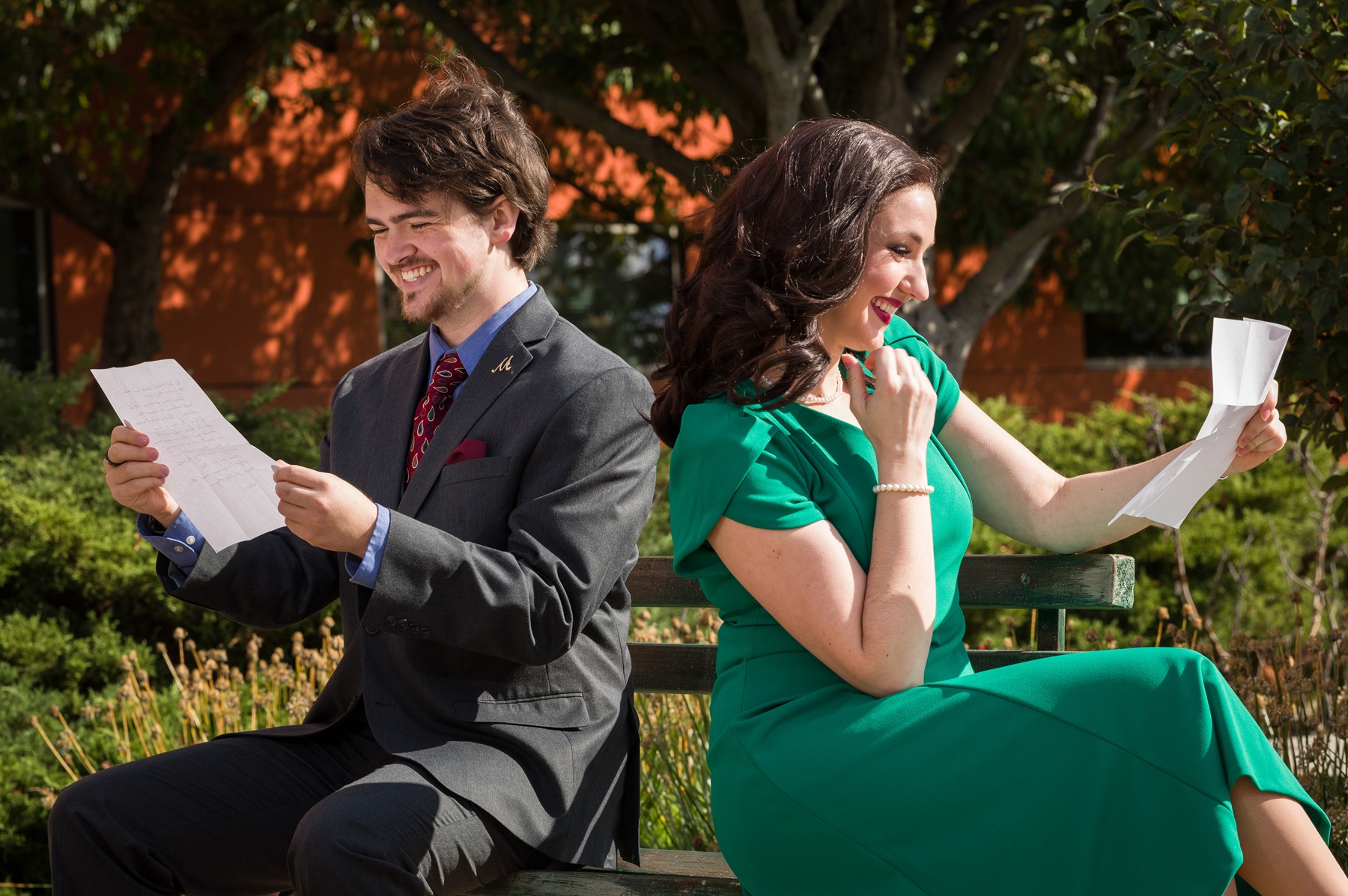 Sam Garrison, as Georg Nowack, and Bethany Brautigam, as Amalia Balash, sit on a bench with their backs to each other while reading love letters 