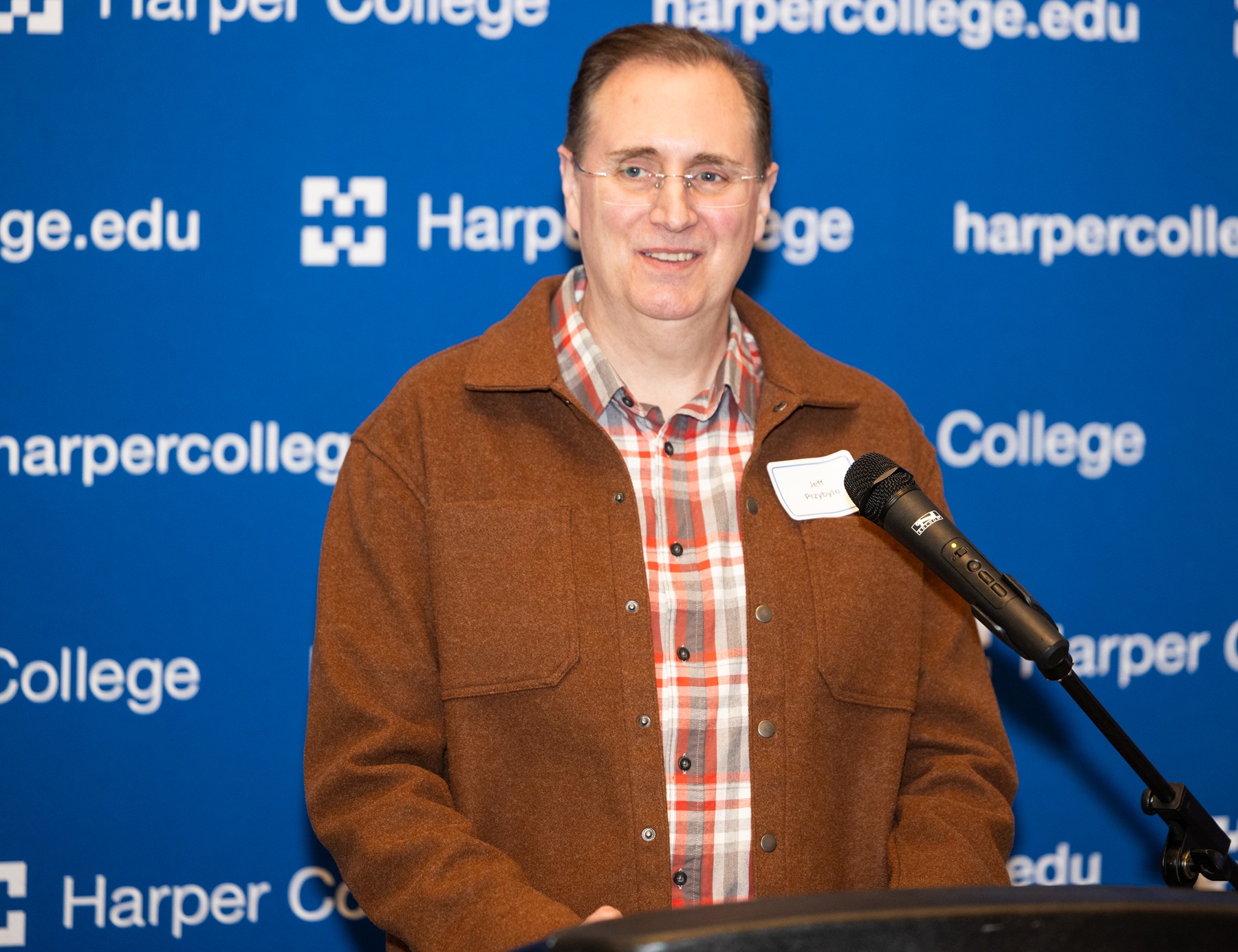 Harper Professor Jeff Przybylo speaks behind a podium at the Speech and Debate Team Reunion