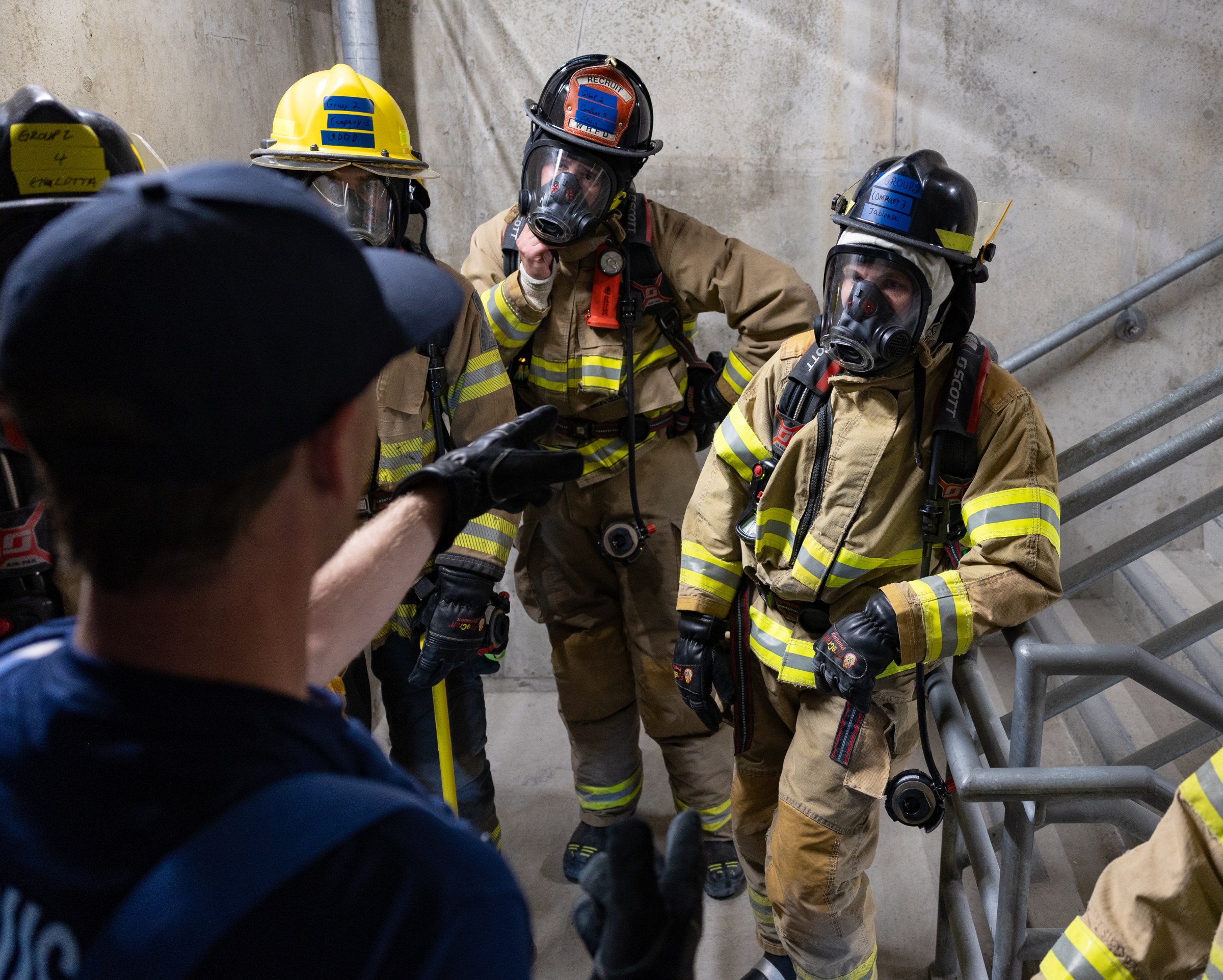 A group of students in firefighter gear stand in a stairwell with an instructor