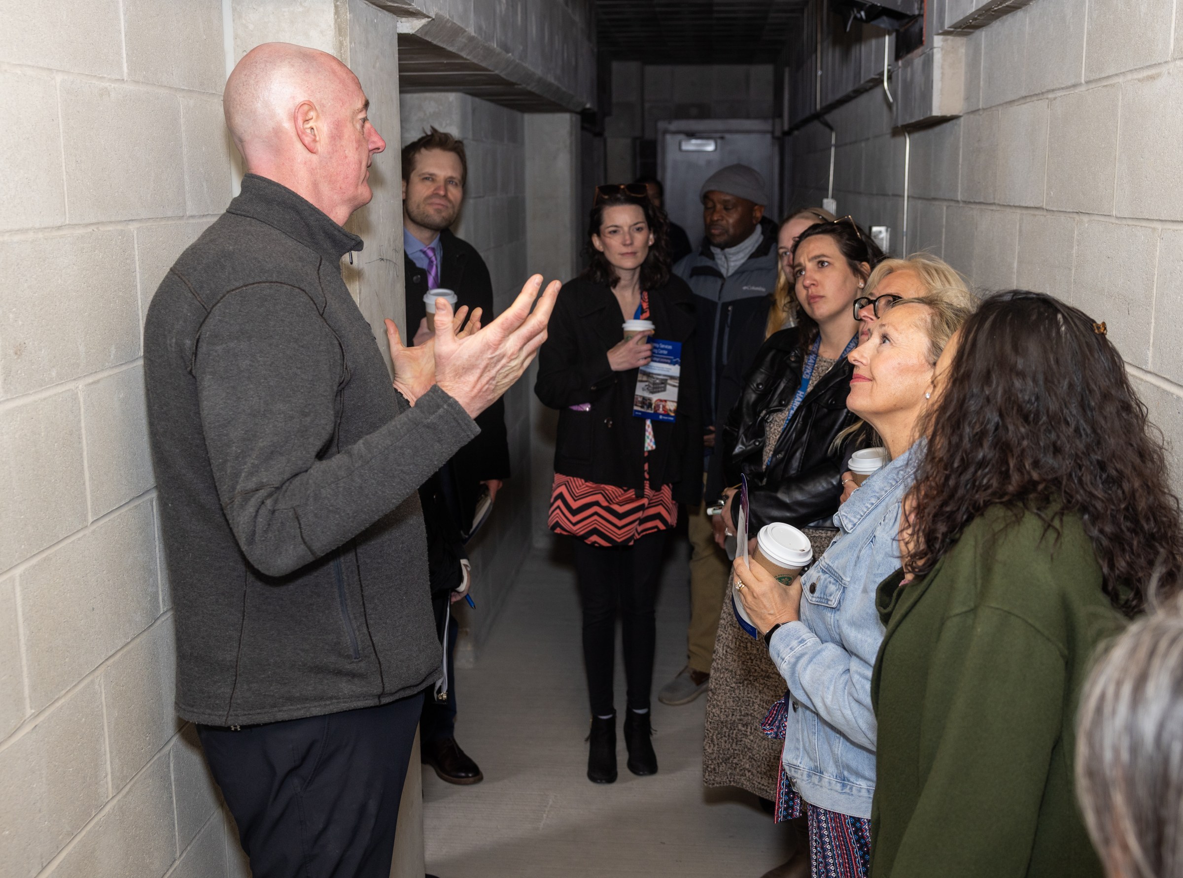 A group of people in a concrete hallway listening to an explanation of the Emergency Services Training Center's features on a tour