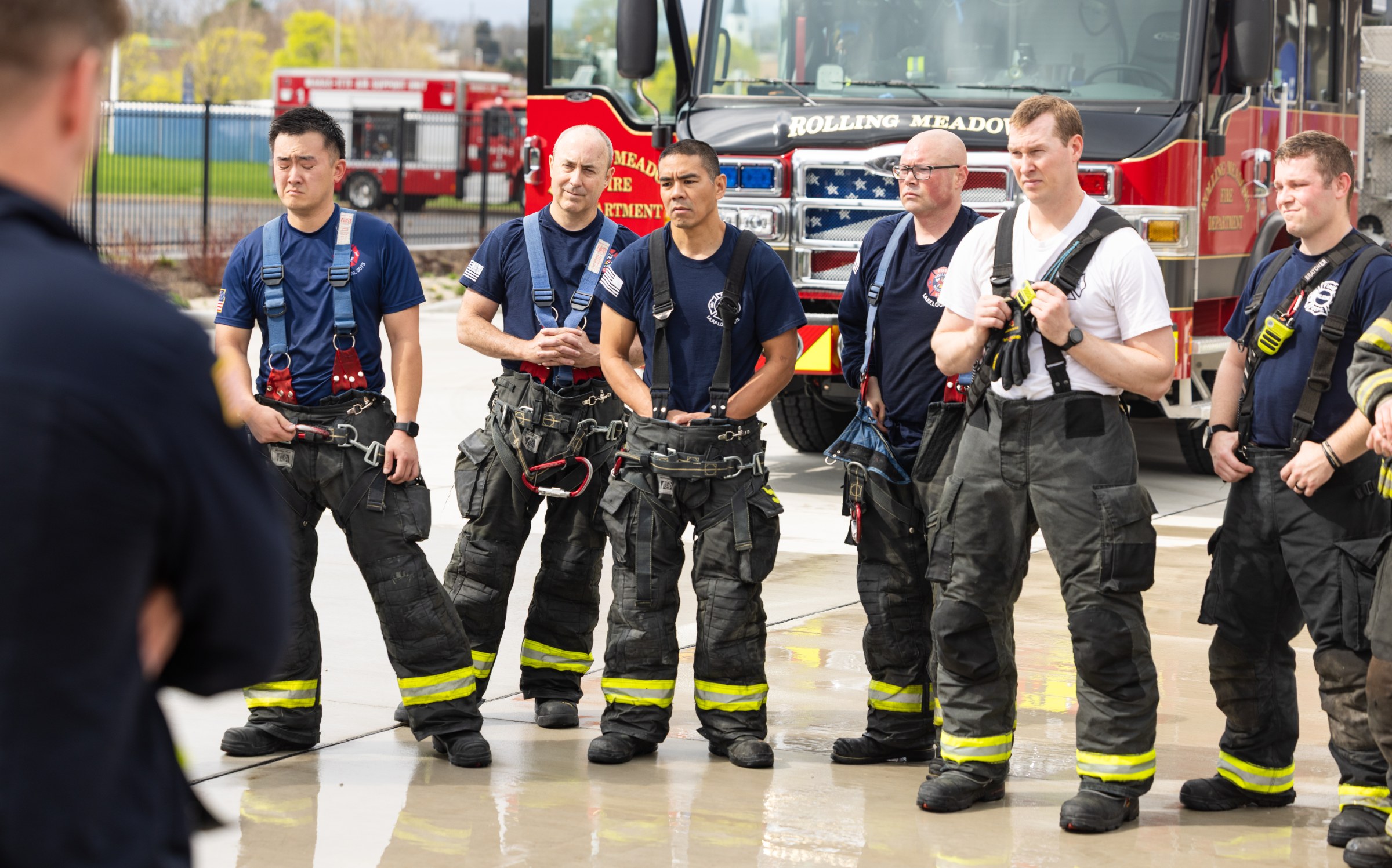 A squad of firefighters from the Rolling Meadows Fire Department stand together in front of a firetruck