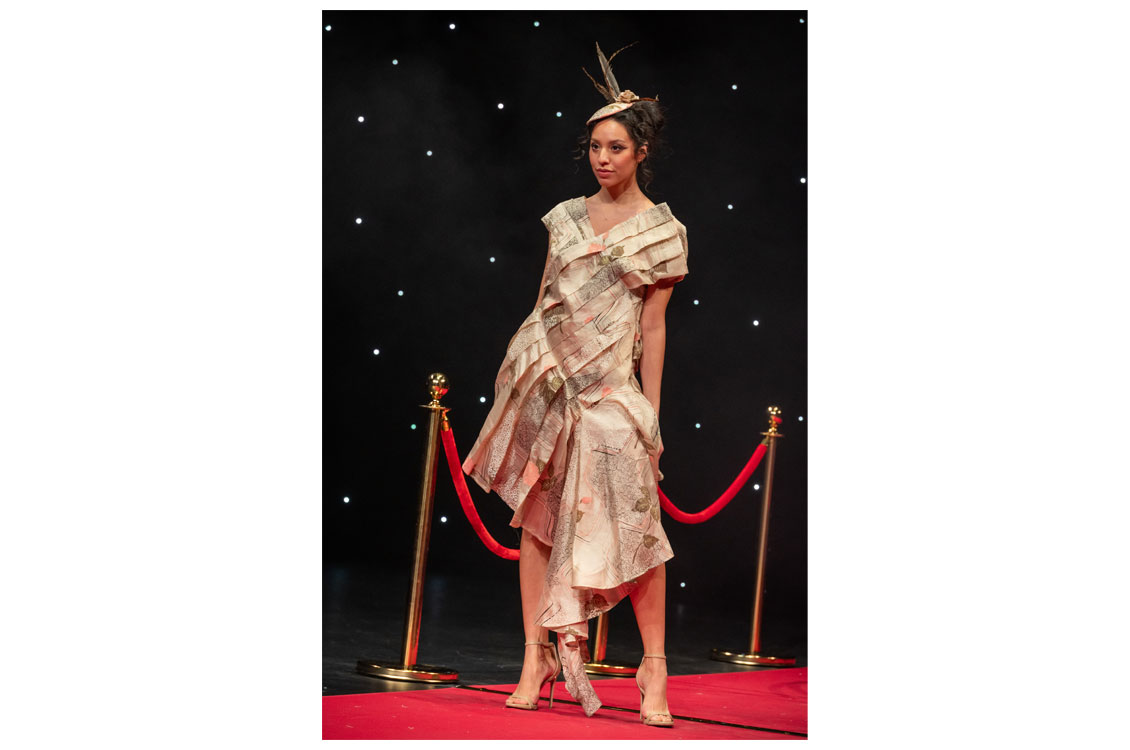 A student wearing a beige dress they created, paired with a matching handcrafted hat they also designed and made.