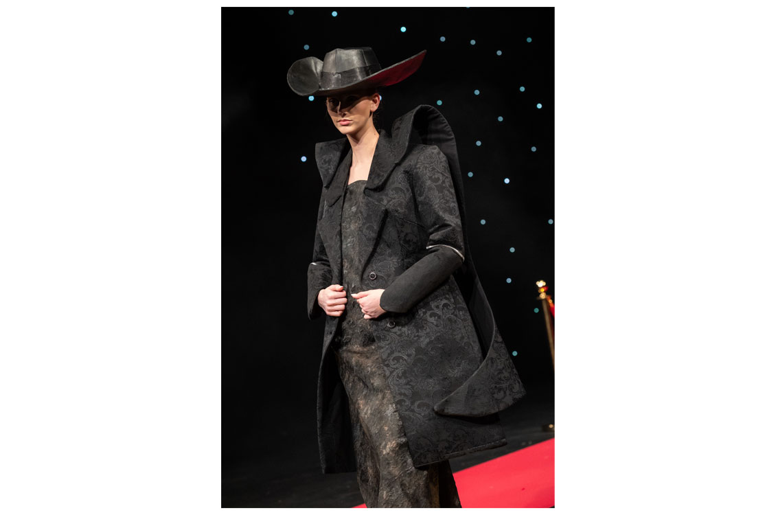 A student models a black dress, jacket, and matching hat they designed and created