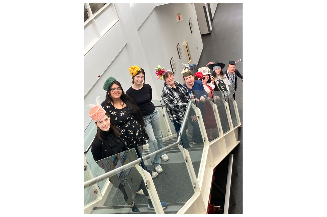 Students standing on a staircase wearing their hat creations.