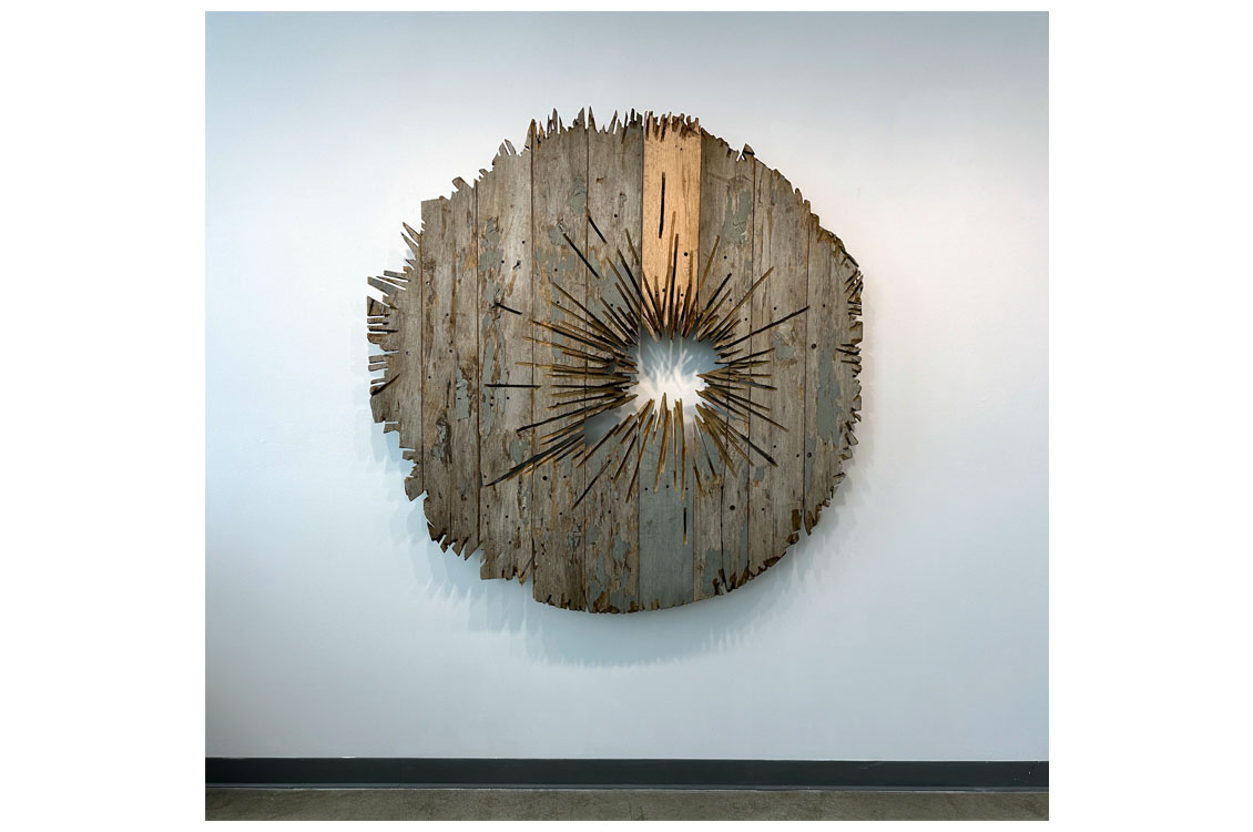 abstract round sculpture made of wood with a hole in the middle, hung on a wall