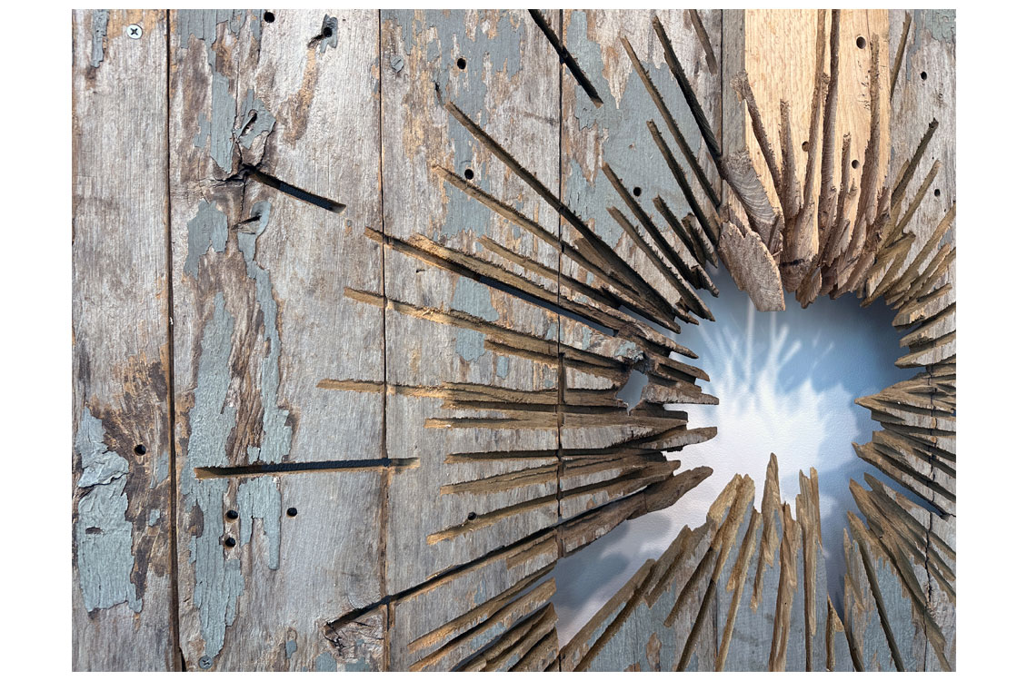 close up of carved hole in wood sculpture with ray-like cuts radiating outward from the center