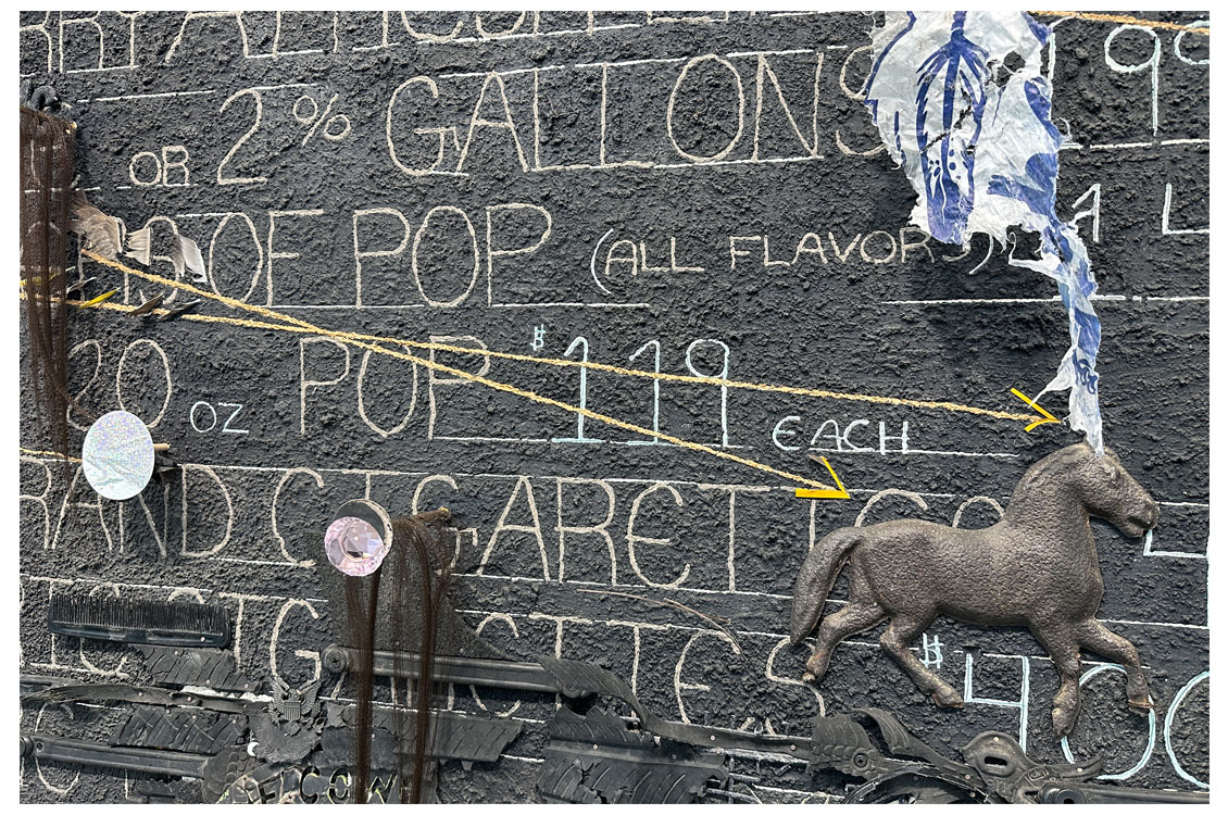 close up of sculpture with words more clear and several items, such as a horse decal, attached to the board