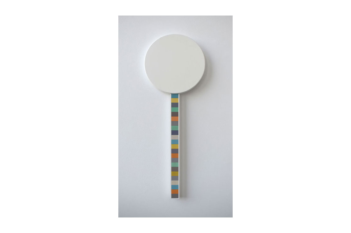 wood sculpture of a white circle with a stick striped in multiple colors