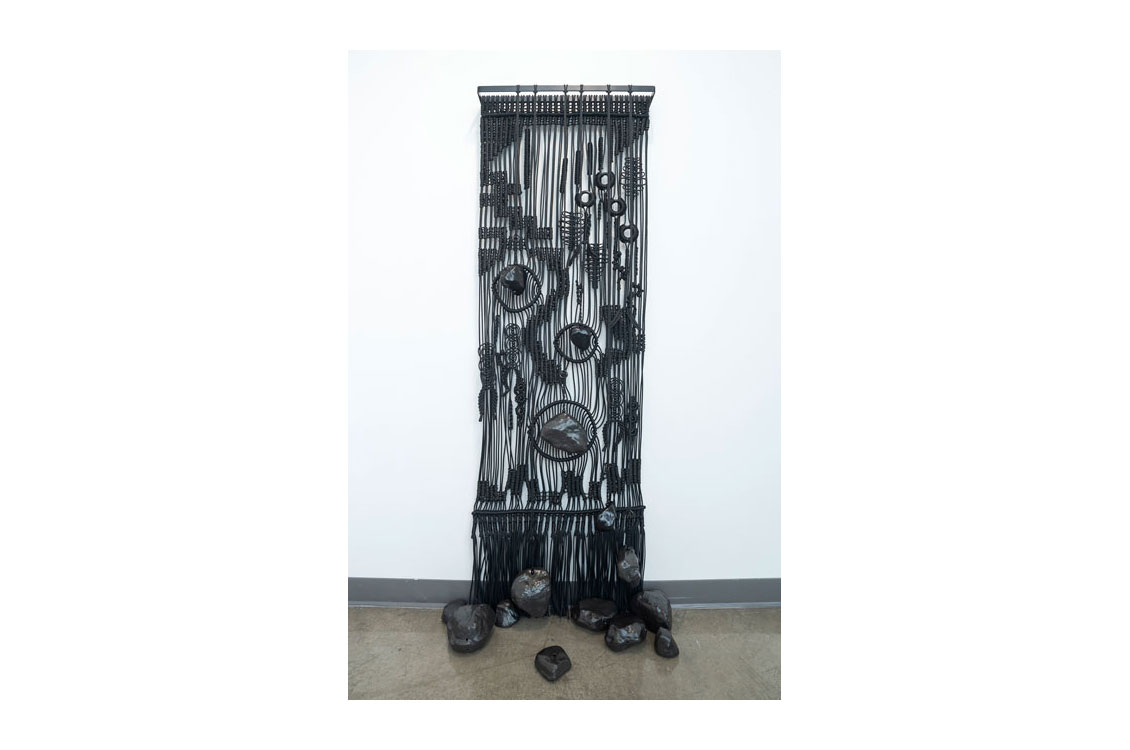 black macramé curtain hung from a rod with rocks at the bottom