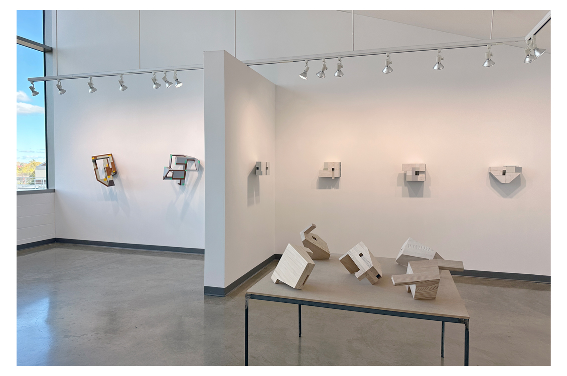 Installation view of wall sculptures with wooden forms on a table.