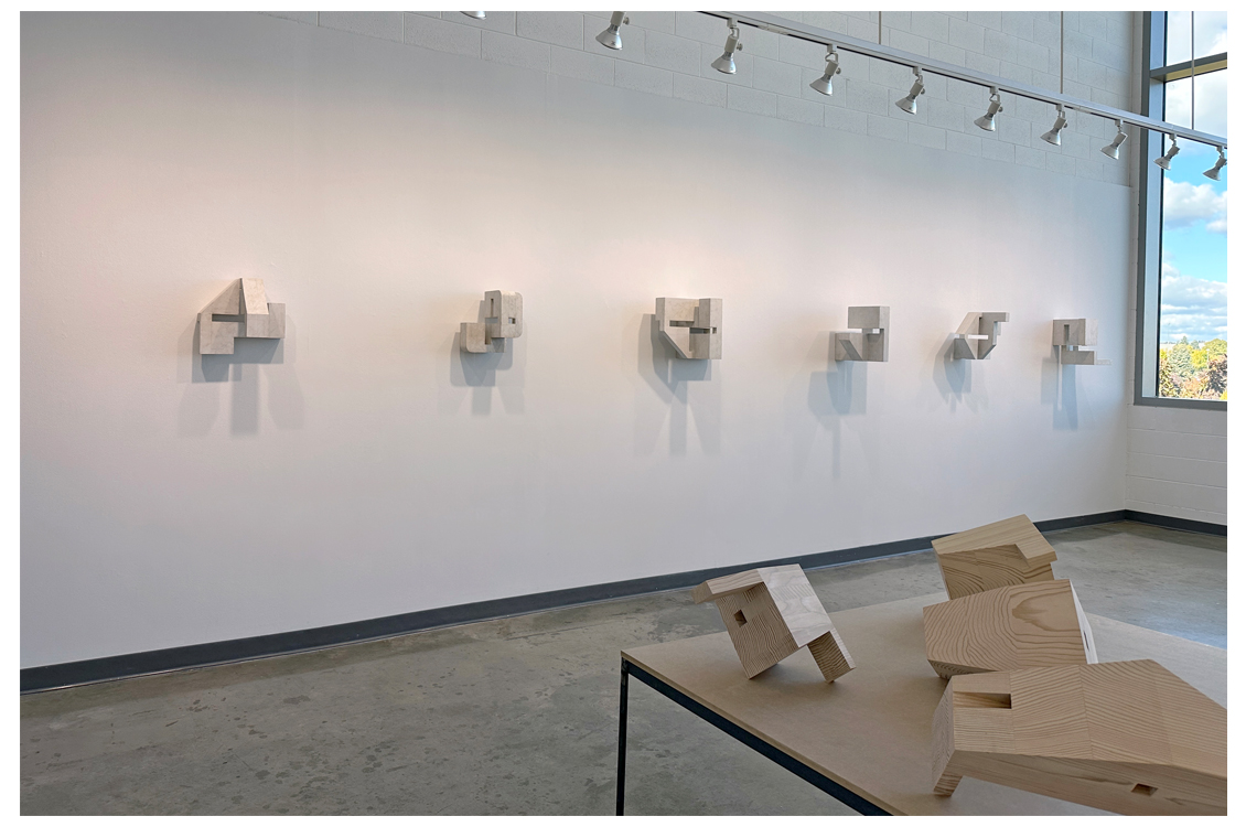 Installation view of pale geometric wall sculptures in a row.
