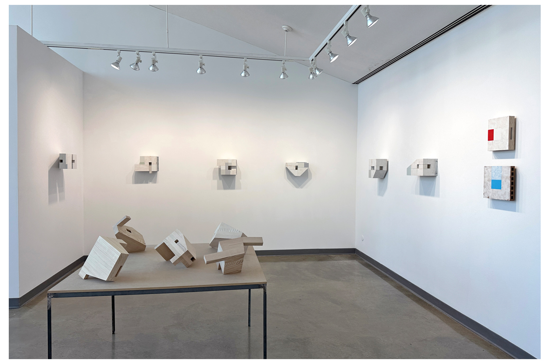 Installation view of pale wall sculptures and wooden forms on a table.