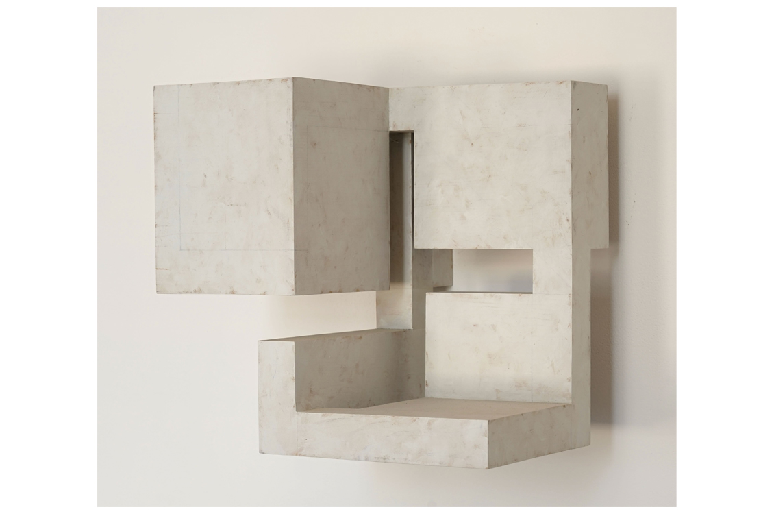 Pale rectangular sculpture with recessed openings and textured surface.