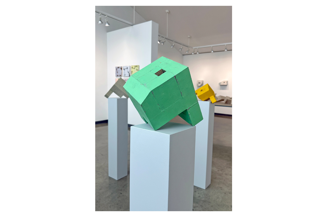 Small green painted wood sculpture tilted on a pedestal.