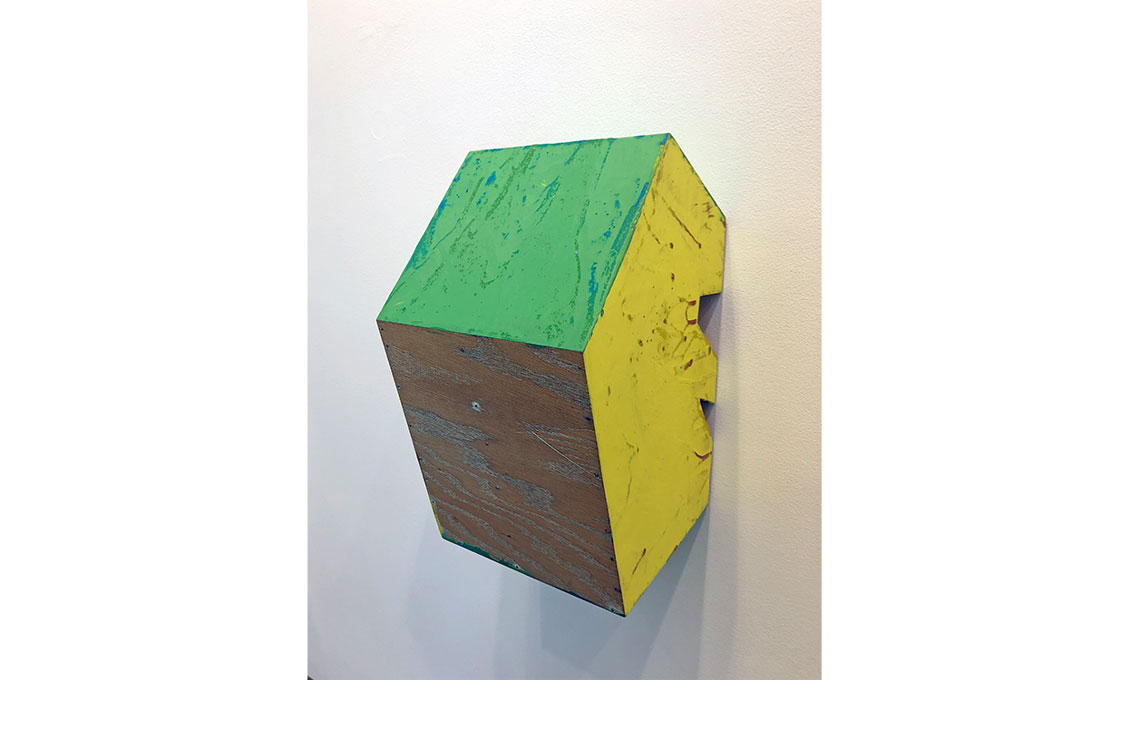 Wood sculpture attached to wall. One side is painted yellow, the other green. 