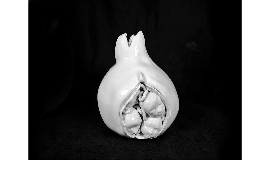 White ceramic sculpture of four baby heads pushing out of a vagina.