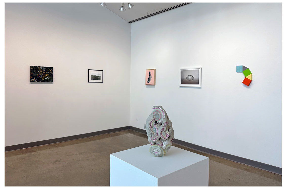 sculpture in foreground with five paintings hanging on the wall in the background