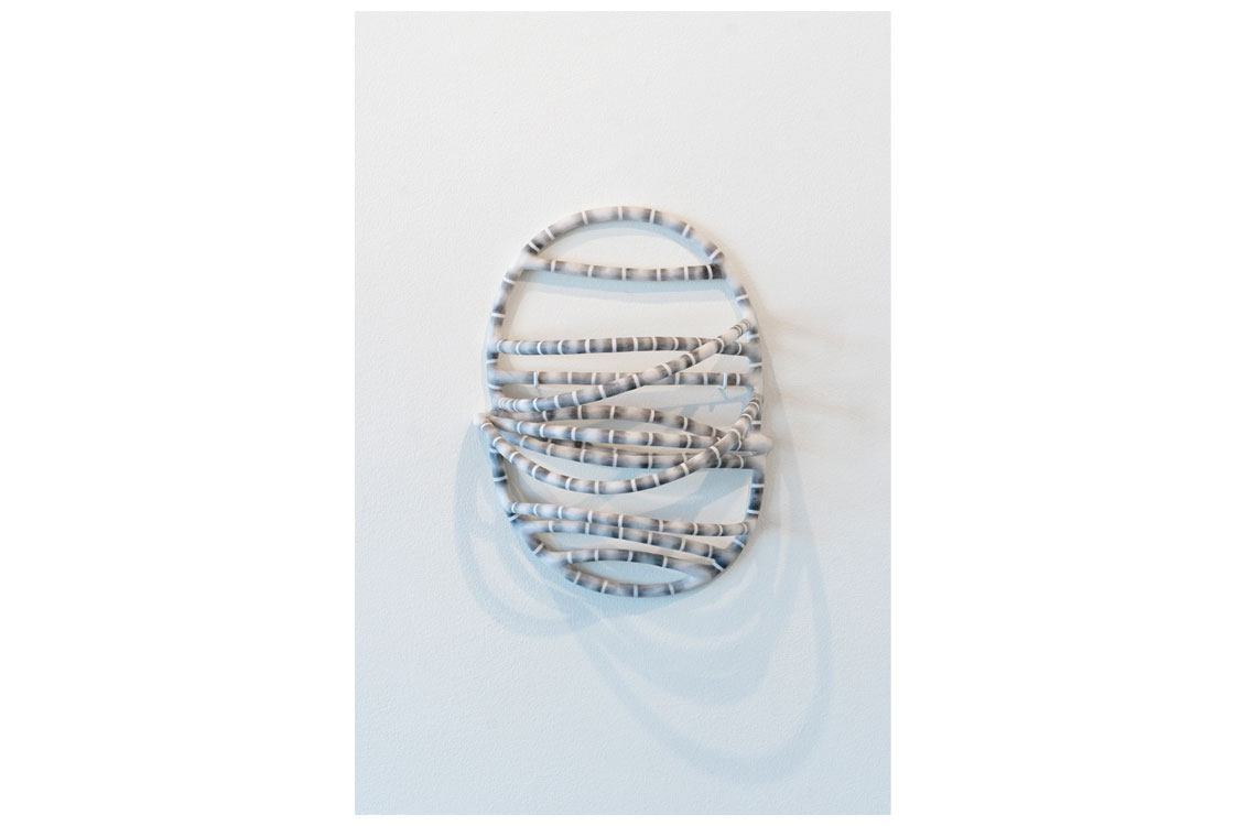 Coiled oval object with alternating light and dark bands, looped on a white surface with visible shadow.