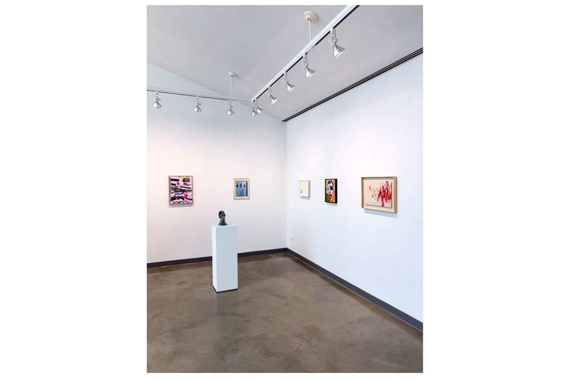 Gallery corner with five framed artworks and a dark textured sculpture on a pedestal.