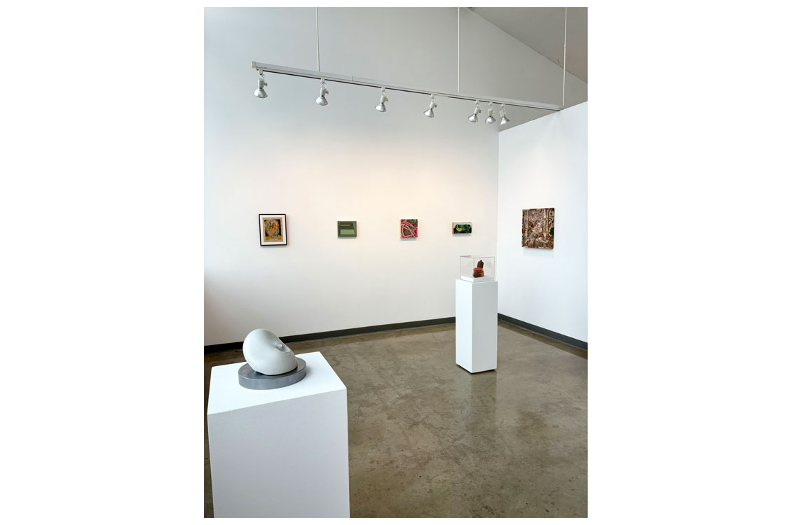 Gallery space with five framed artworks and two sculptures displayed on pedestals.
