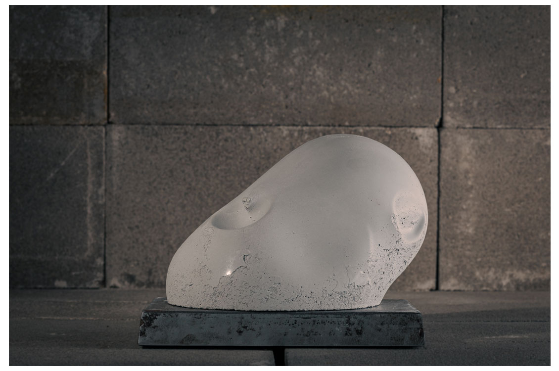 Smooth, pale abstract sculpture resembling a rounded stone form on a dark pedestal.
