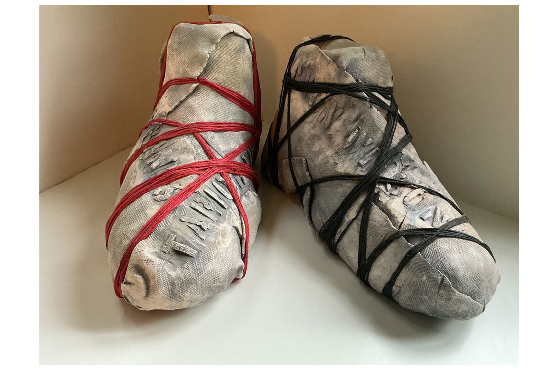 Two soft sculptural forms resembling wrapped feet, bound with red and black string.