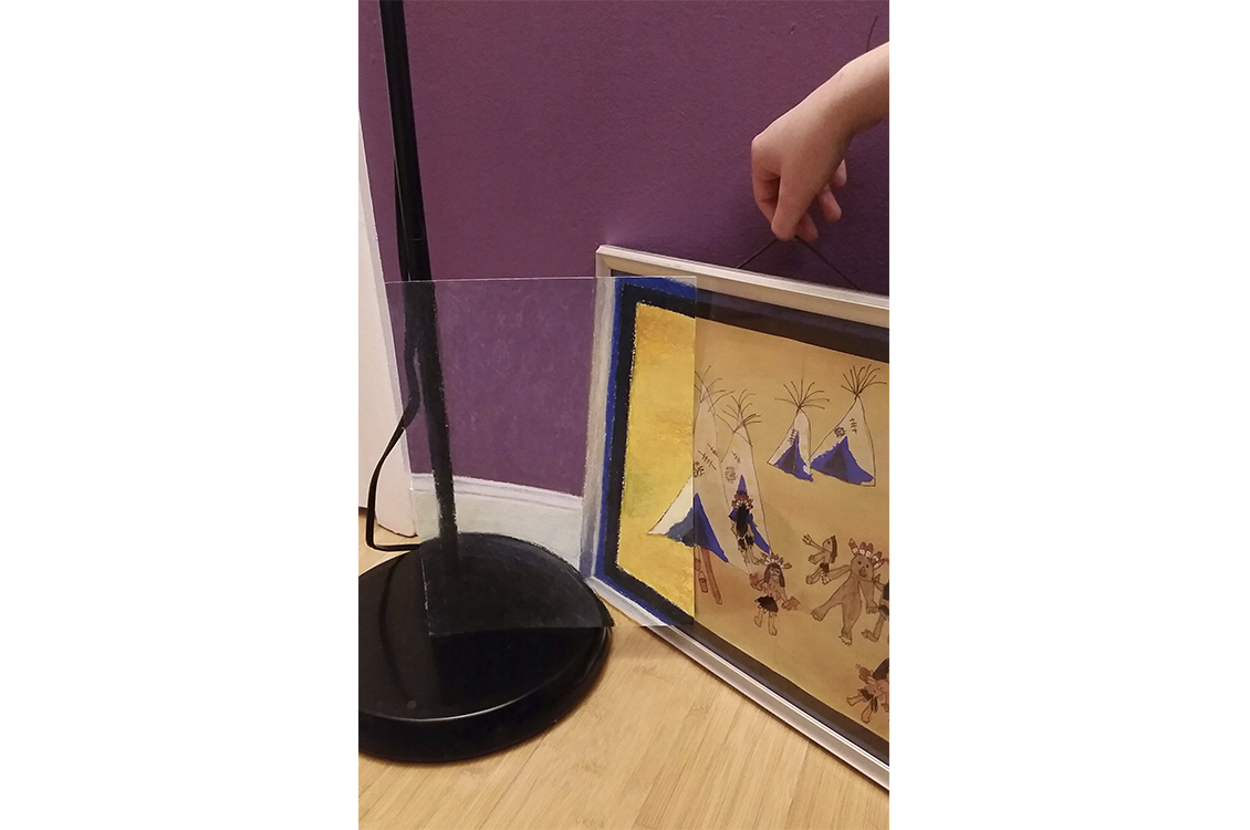 photo of a hand holding a painting next to a lamp