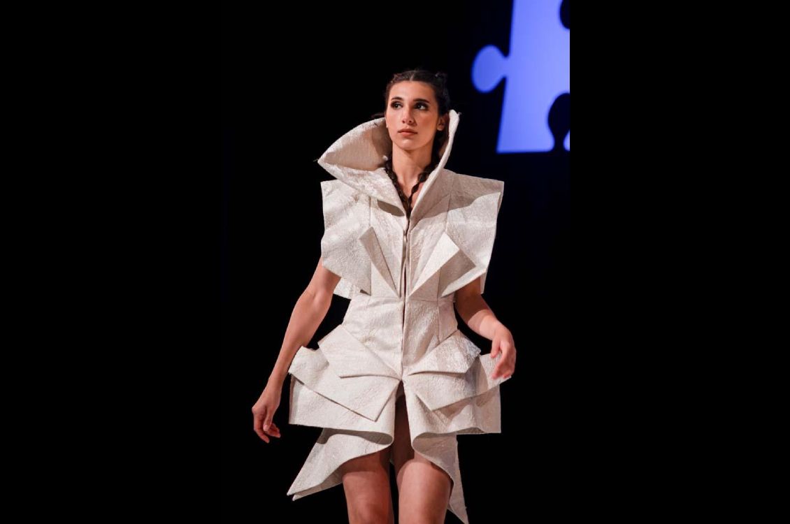 Female model wearing a textured cream colored dress. The fabric that is folded like origami