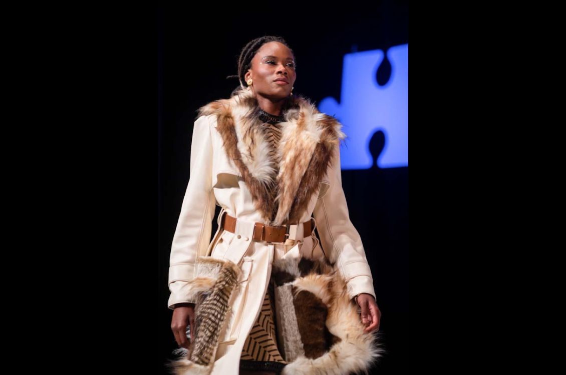 Model wearing a long cream colored coat with fur accents.