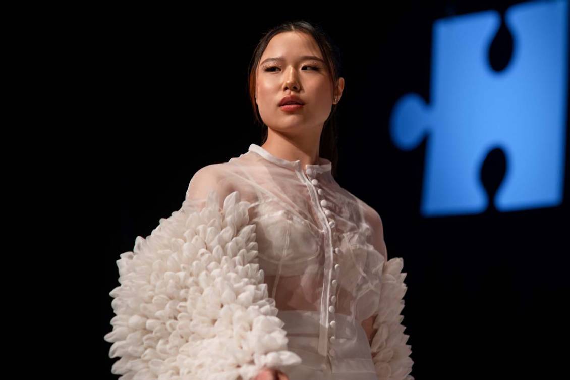 Model wearing a sheer white blouse with heavily puffed sleeves textured like flower petals