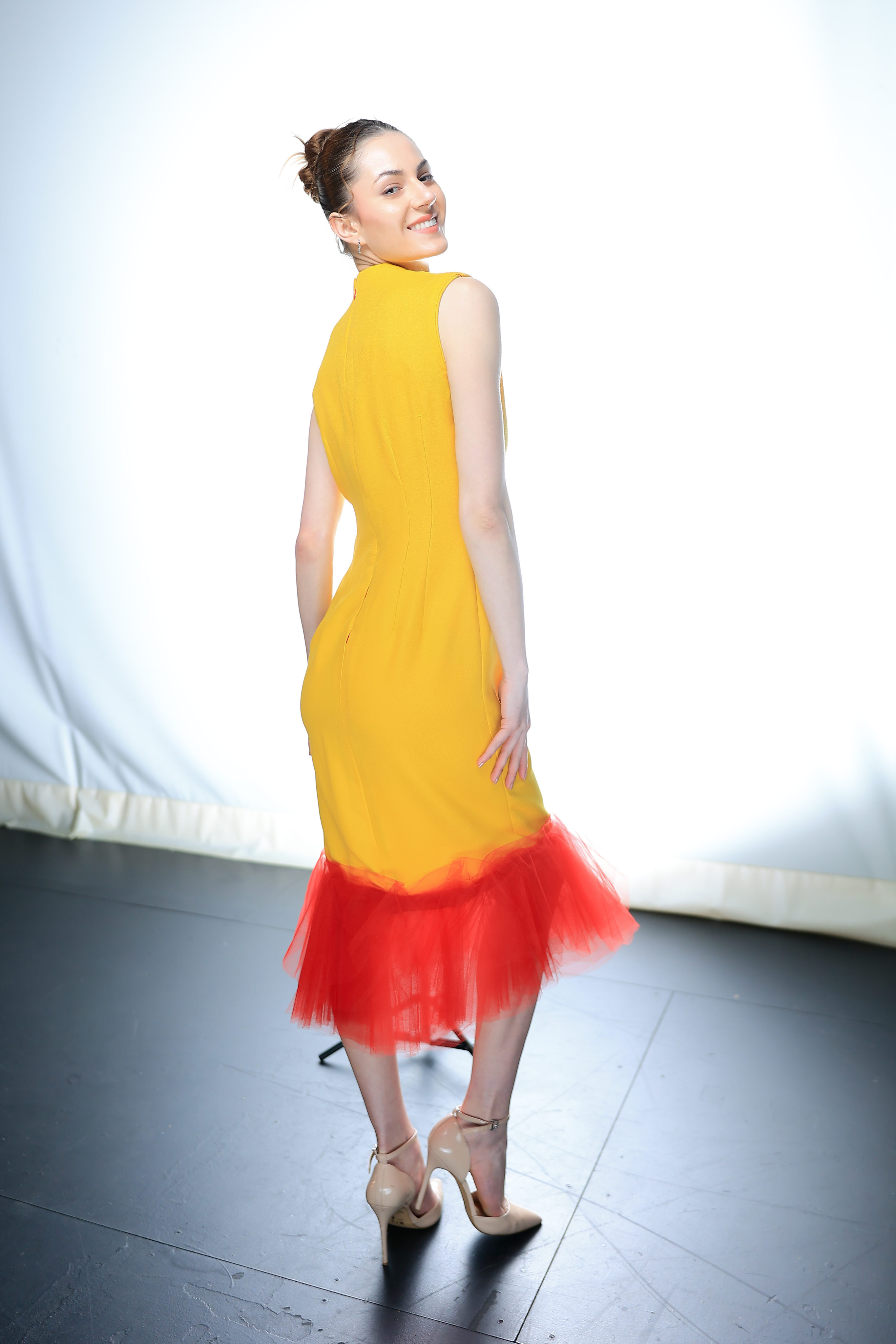 Model posed for photos, wearing beige heels and a yellow and red sleeveless dress
