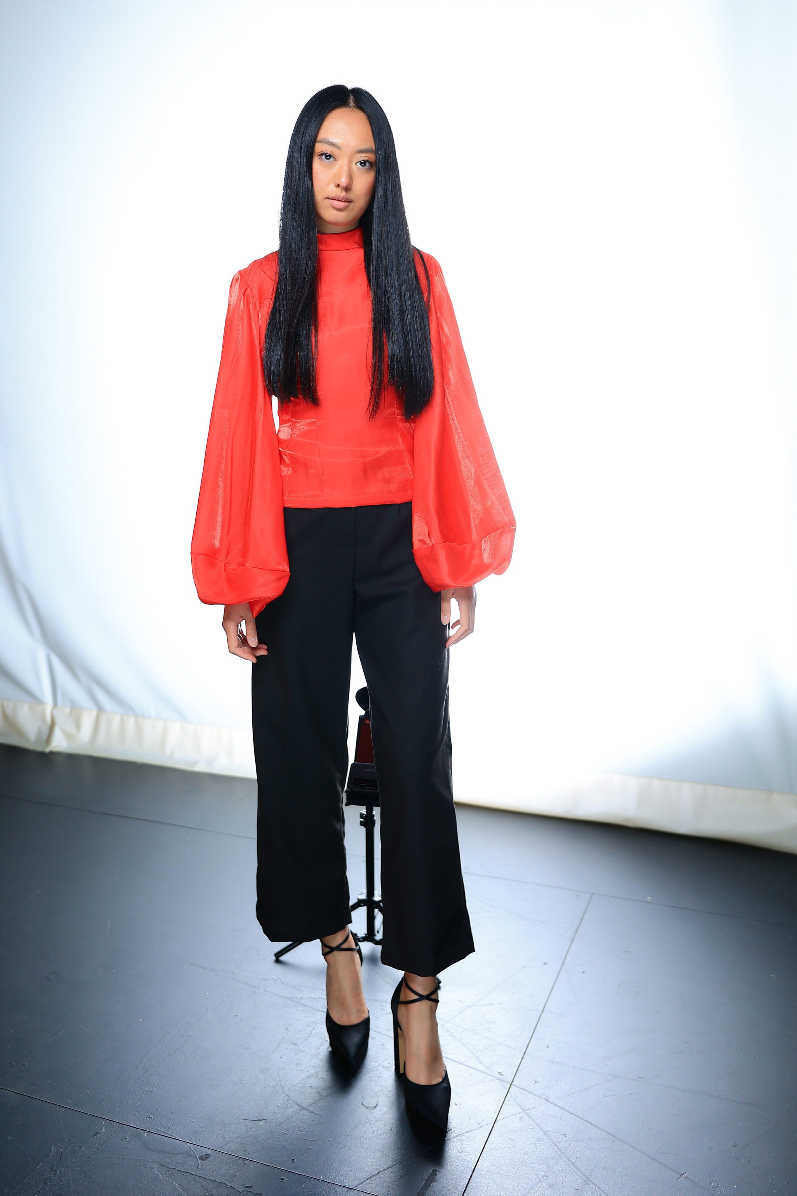 Model posing for photos wearing a red long sleeved top, black wide legged slacks and black heels.