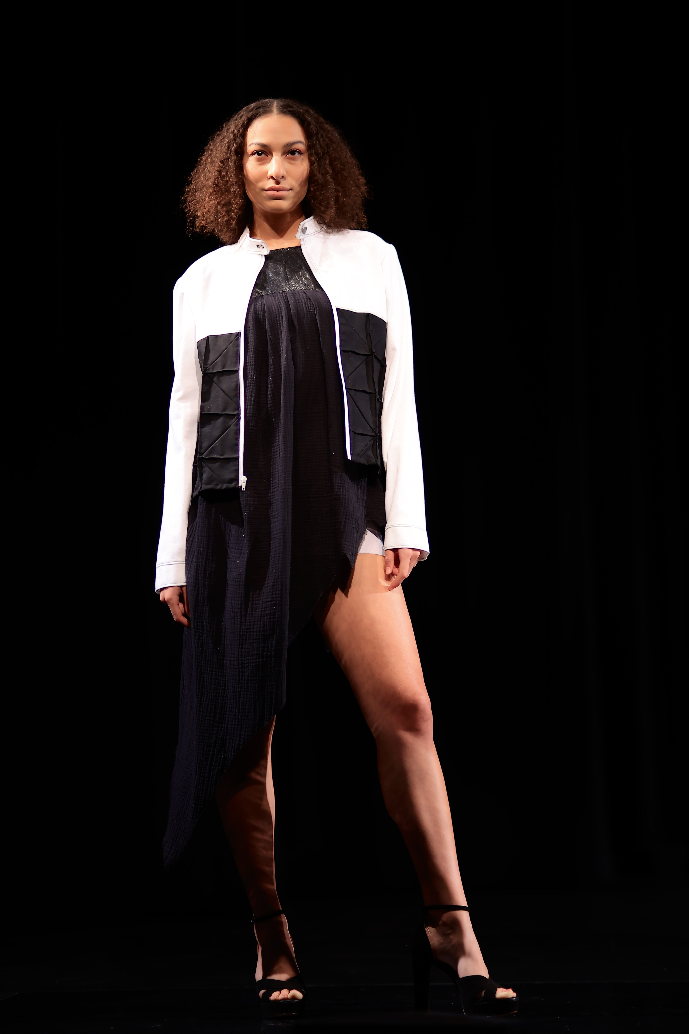 A model dress in a black dress, black heels, and a white and black jacket.