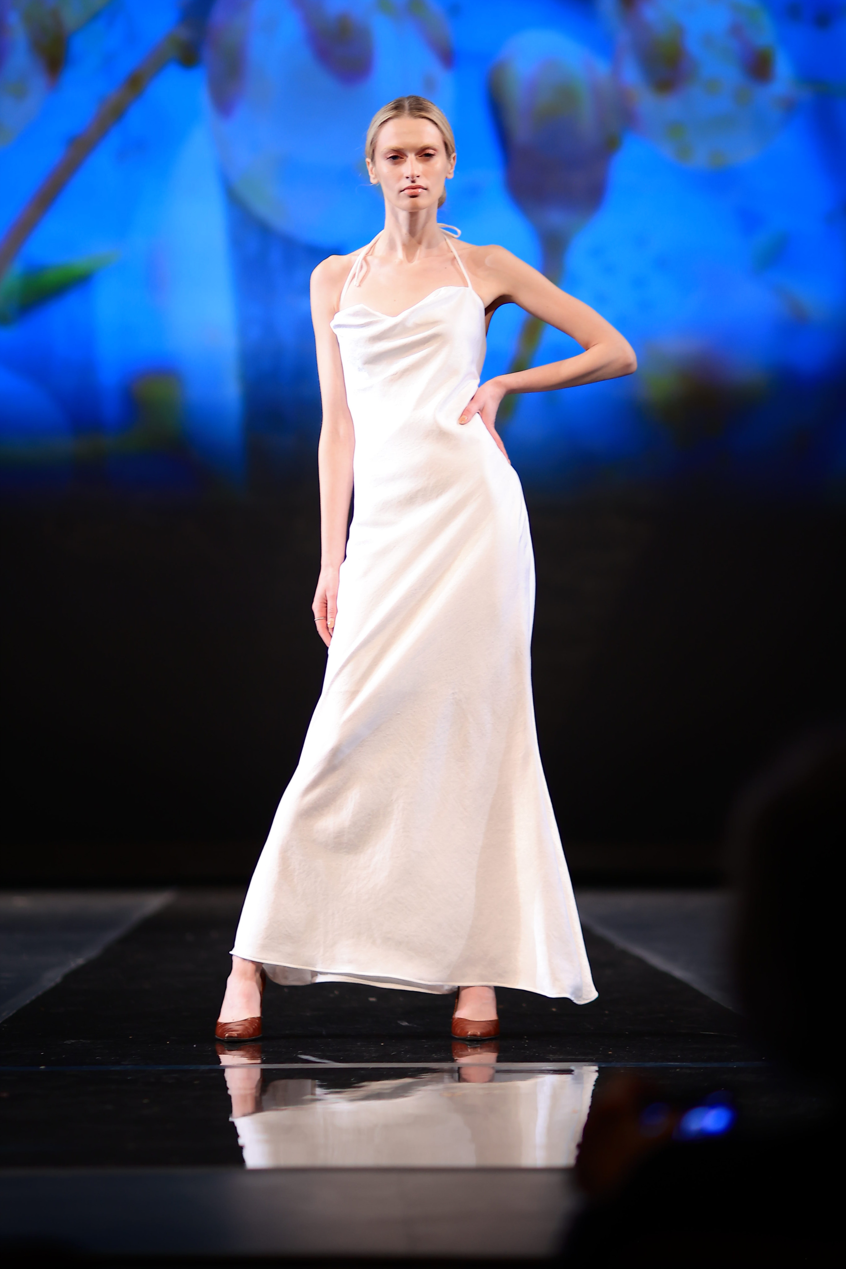 Model wearing a long white dress and brown heels with their hair up in a low bun.