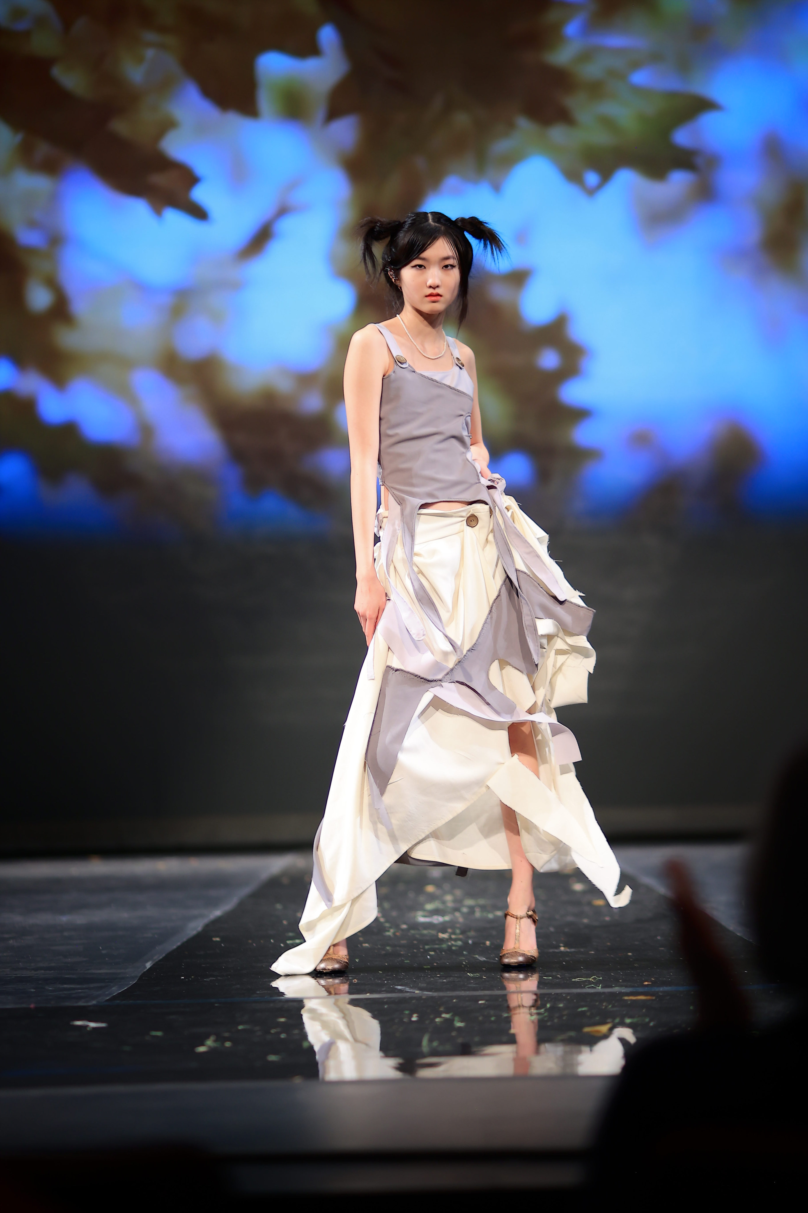 A model posing on  the runway wearing a light gray and white two-piece sleeveless dress.