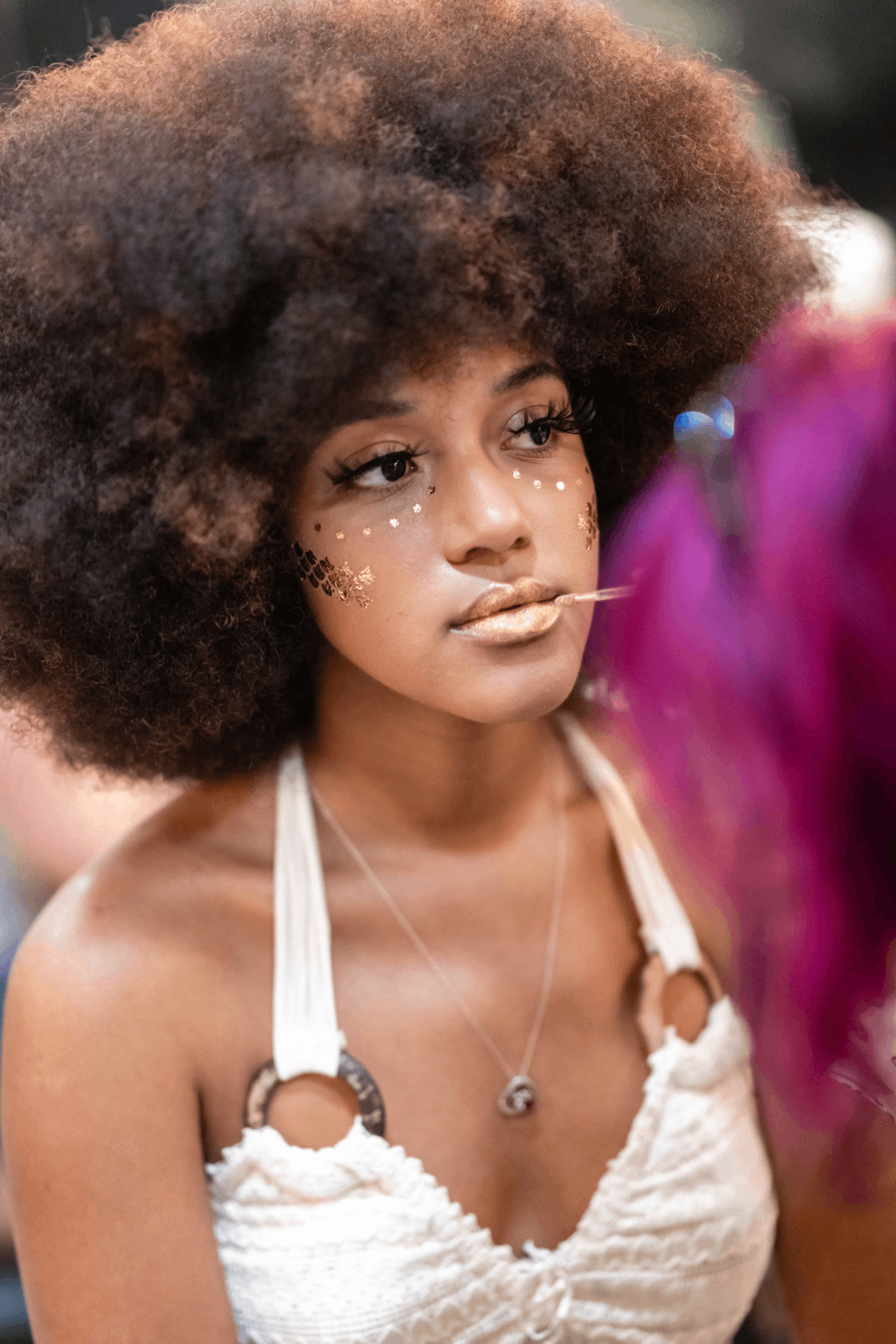 A model getting shimmery gold lip gloss painted on her lips backstage